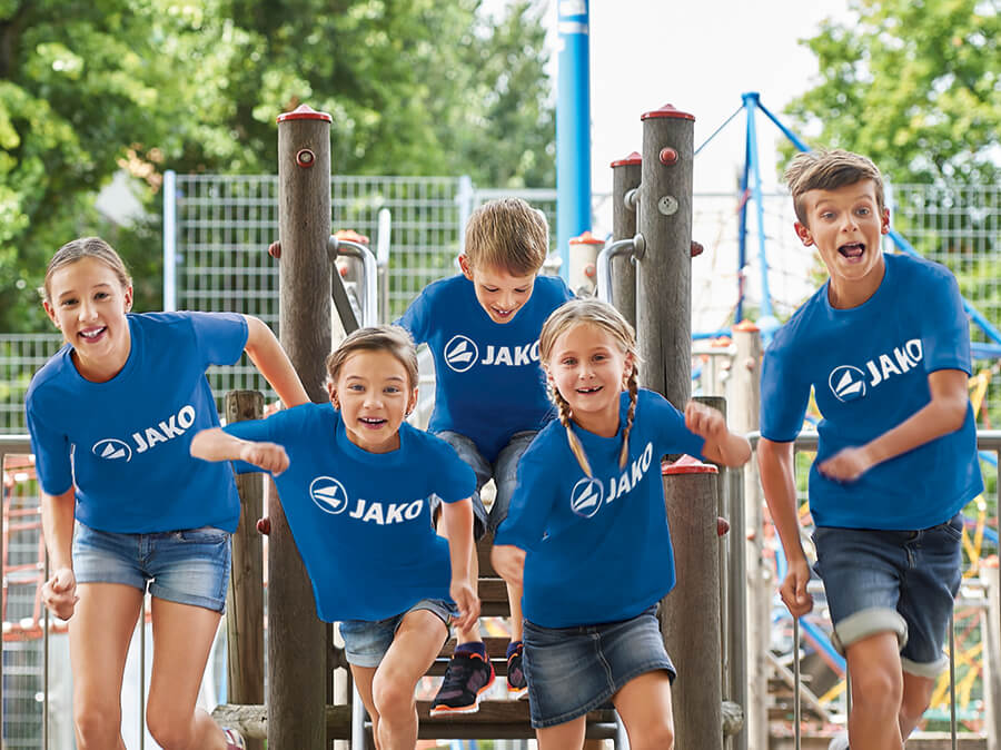 Een groep kinderen met JAKO T-shirts speelt in de speeltuin.
