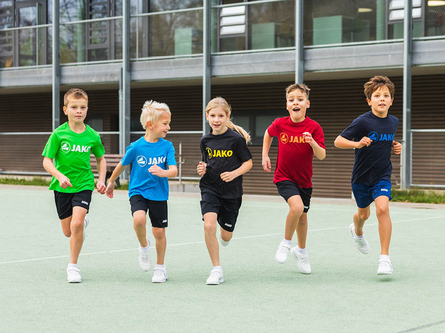 Un groupe d'enfants portant des T-shirts JAKO jouent dans la cour de récréation.